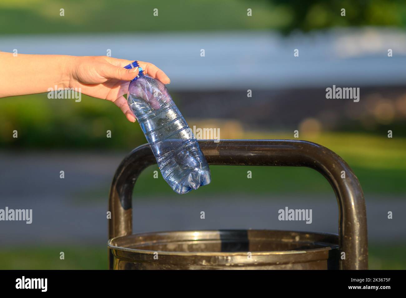 A woman throws plastic bottles into a trash can in a city park Stock ...