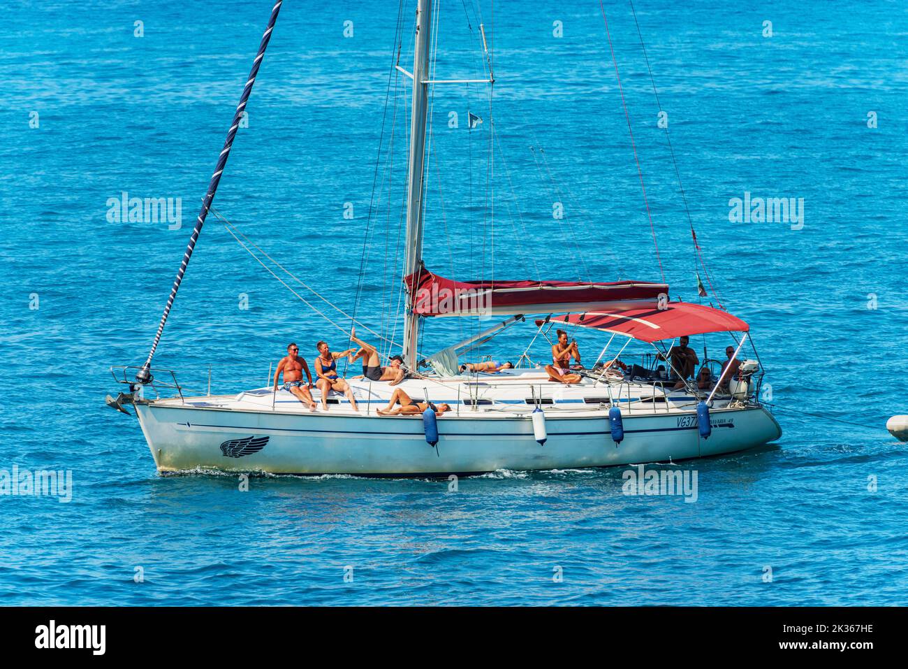 White sailboat with a group of people on board, in front of the Tellaro village, Lerici, Mediterranean Sea, Gulf of La Spezia, Liguria, Italy, Europe. Stock Photo