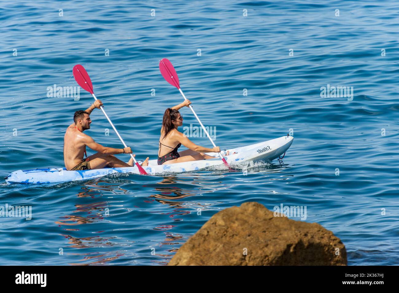 A young couple, a man and a woman in a bathing suit paddle in the blue Mediterranean sea on a kayak, on a sunny summer day. Gulf of La Spezia, Liguria Stock Photo