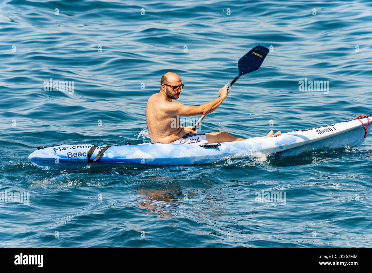 Adult man, 40-45 years paddle in the blue Mediterranean sea on a blue kayak on a sunny summer day. Tellaro, Lerici, Gulf of La Spezia, Liguria, Italy. Stock Photo