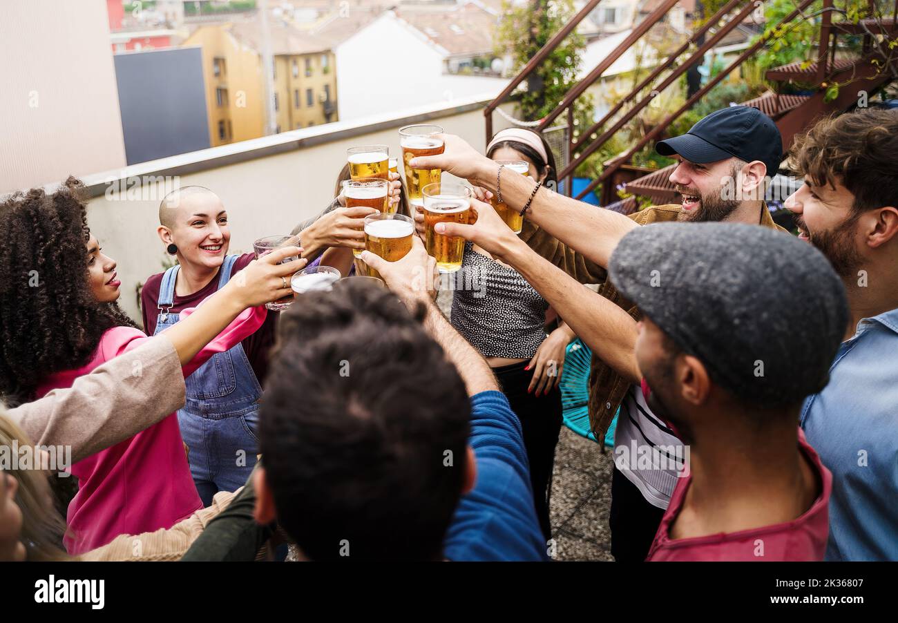 multiracial friends celebrating with a toast clinking beers standing together at the rooftop party - group of young people having fun in the terrace - Stock Photo