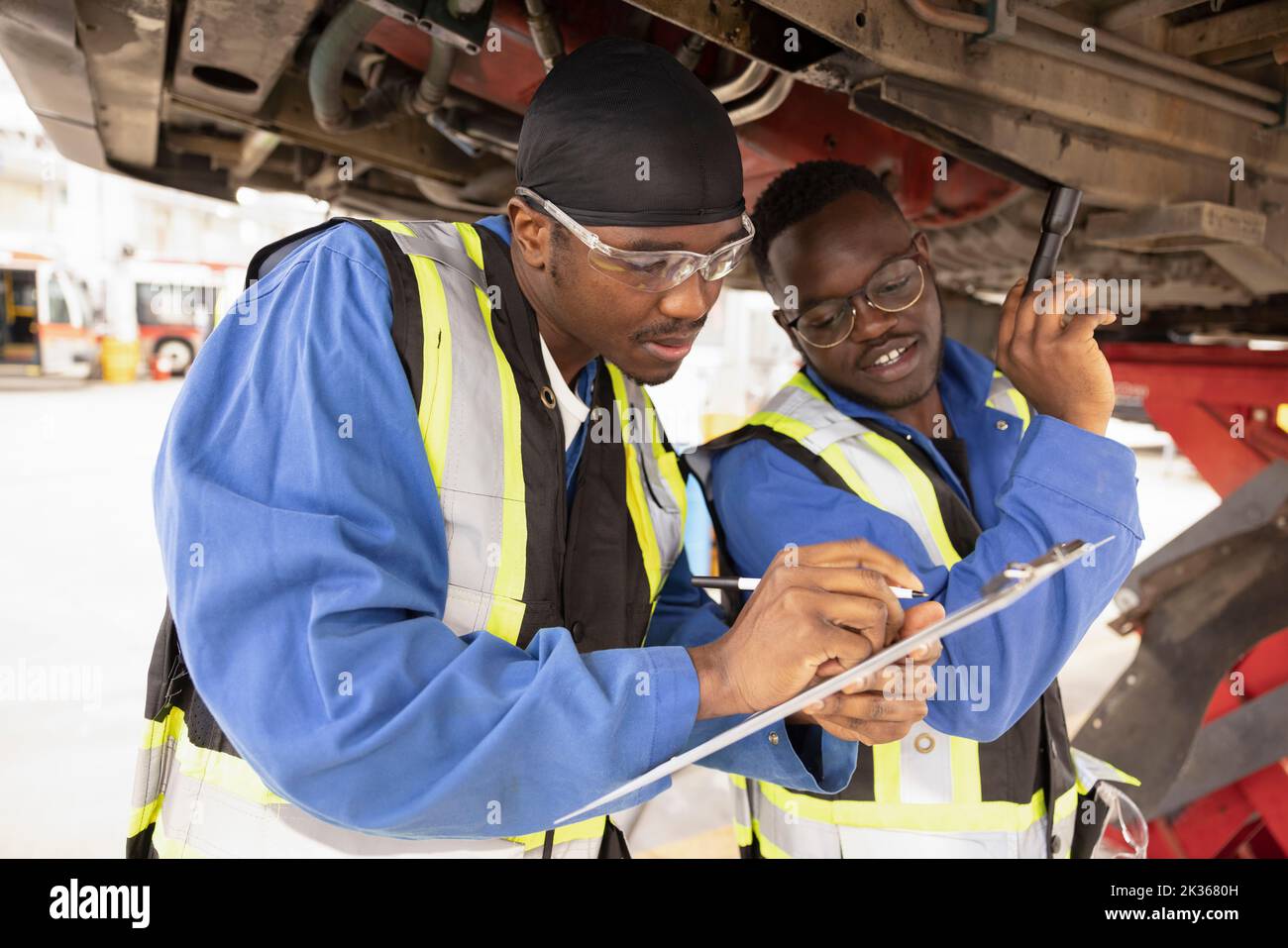 Male mechanics with clipboard under bus in maintenance facility Stock