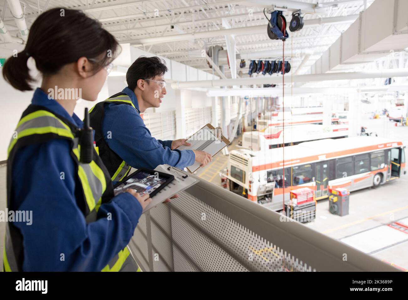 Workers with clipboard on platform in bus maintenance facility Stock