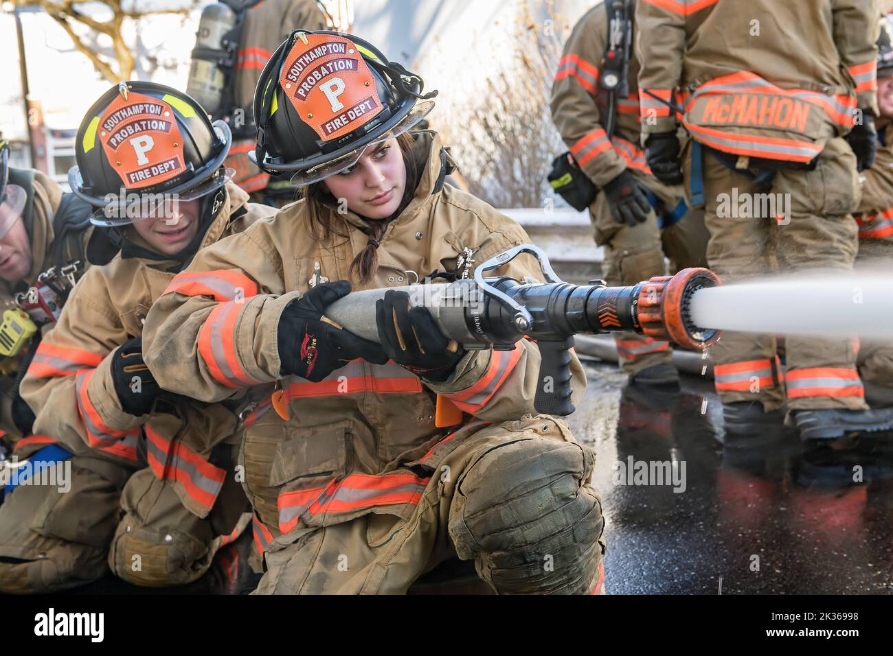 A female probationary firefighter gets practice handling the nozzle of a fire hose as the Southampton Fire Department, assisted by units and members f Stock Photo