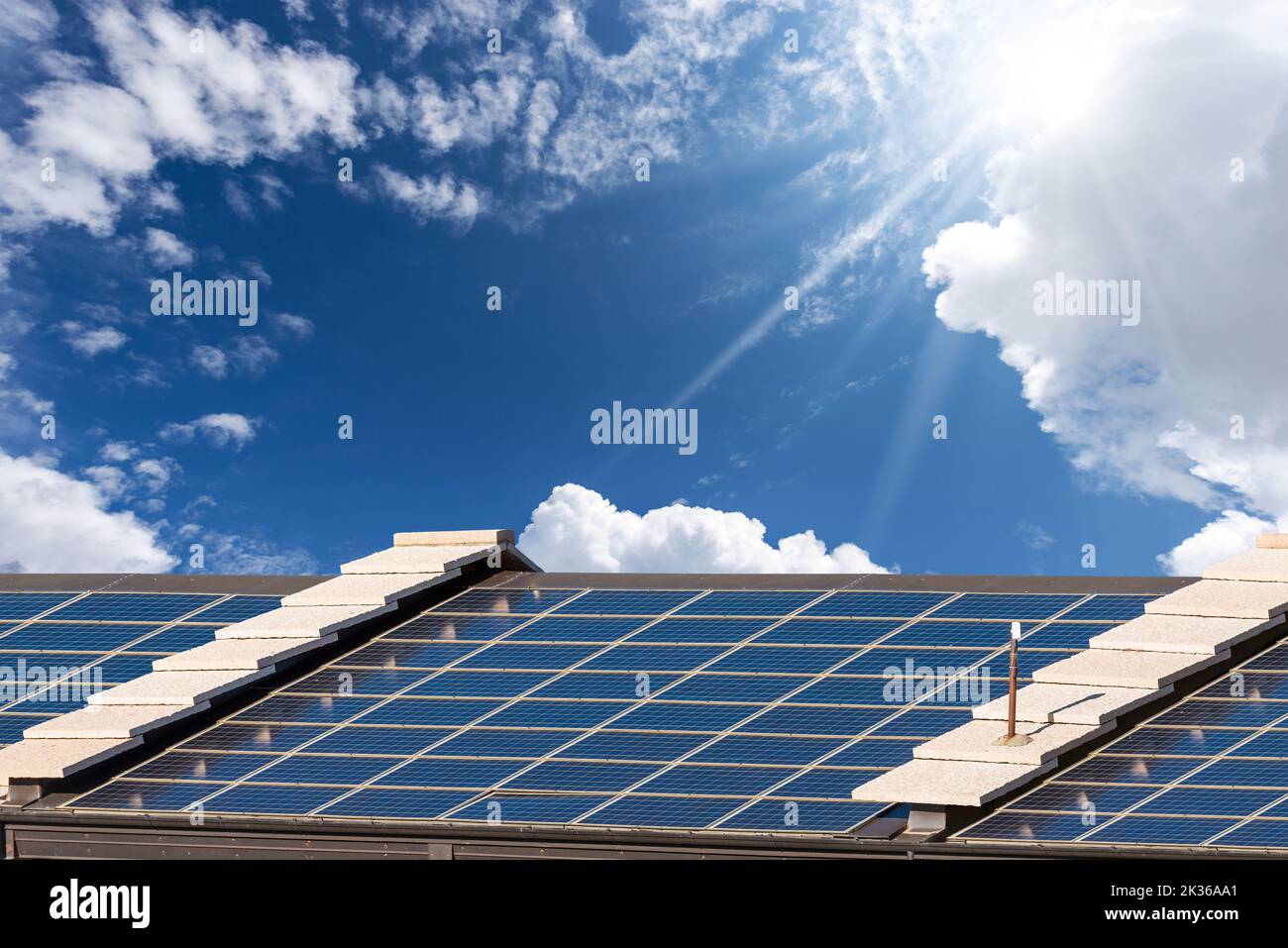 Close-up of a roof with many solar panels against a clear blue sky with clouds, sunbeams and copy space. Veneto, Italy, Europe. Stock Photo
