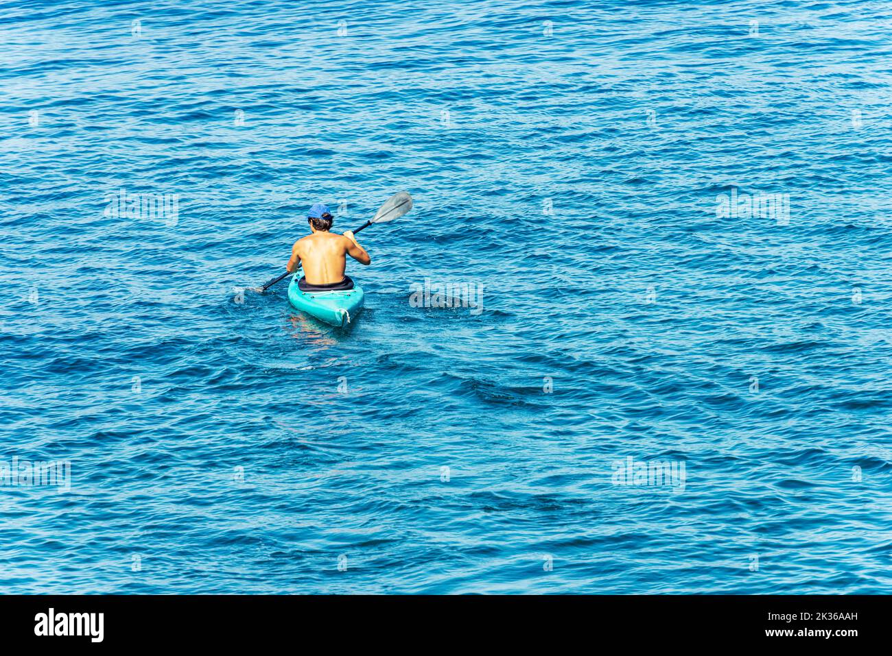Young adult man, 30-35 years, paddle in the blue Mediterranean sea on a kayak. Tellaro village, Lerici municipality, Gulf of La Spezia, Liguria, Italy Stock Photo