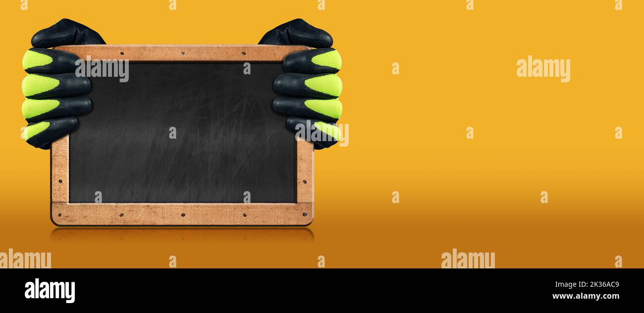 Manual worker with protective work gloves holding a blank blackboard with wooden frame, on a yellow and orange background with copy space. Stock Photo