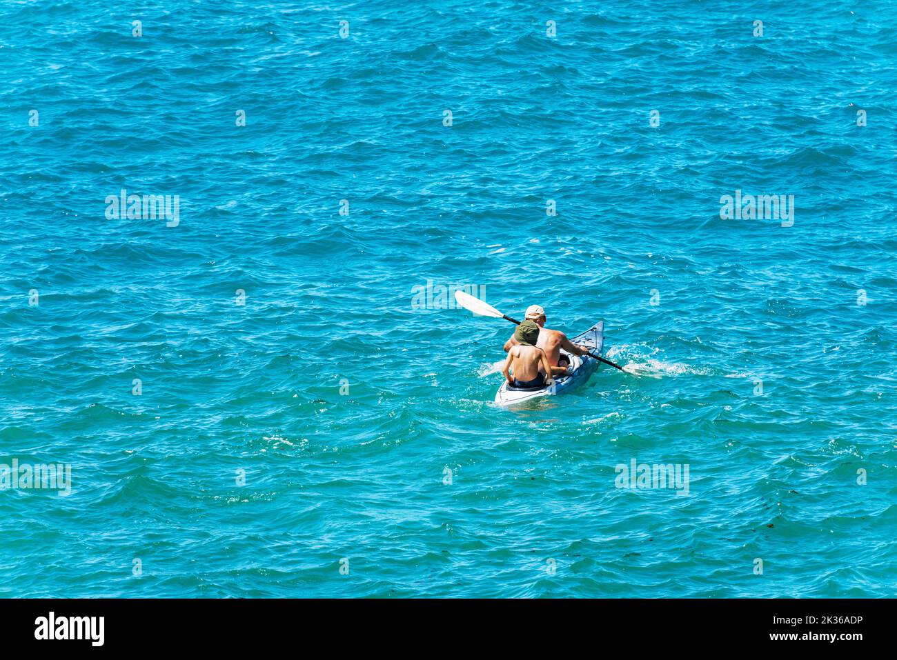 An adult man and a little boy paddle in the blue of the Mediterranean Sea on a kayak. Tellaro village, Lerici, Gulf of La Spezia, Liguria, Italy. Stock Photo