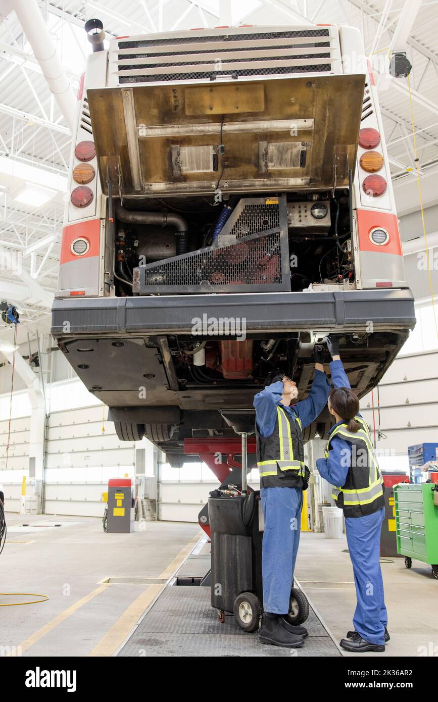 Mechanics working under bus in maintenance facility Stock Photo - Alamy