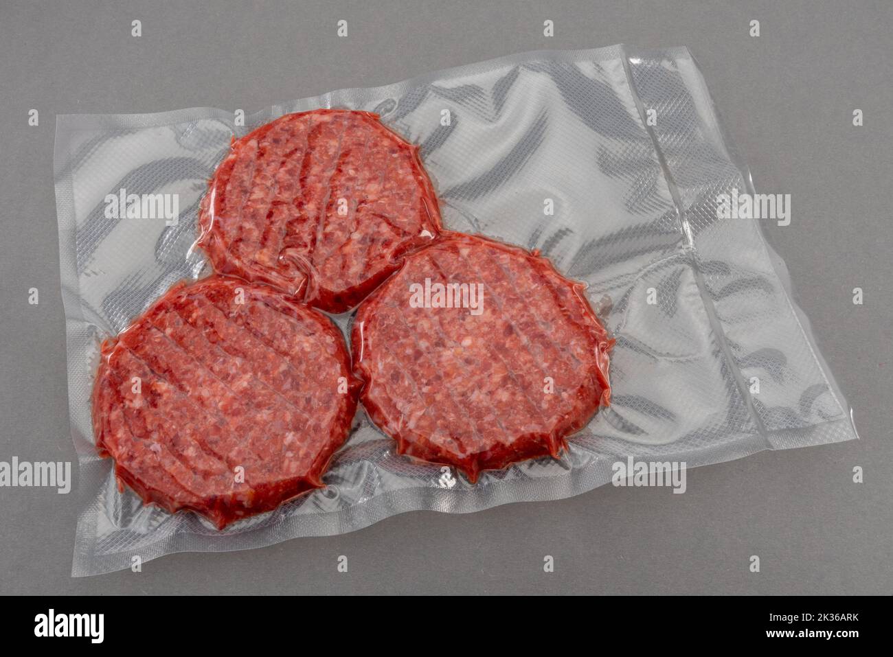 Raw burger meat for hamburger in vacuum packed sealed for sous vide cooking isolated on gray background Stock Photo