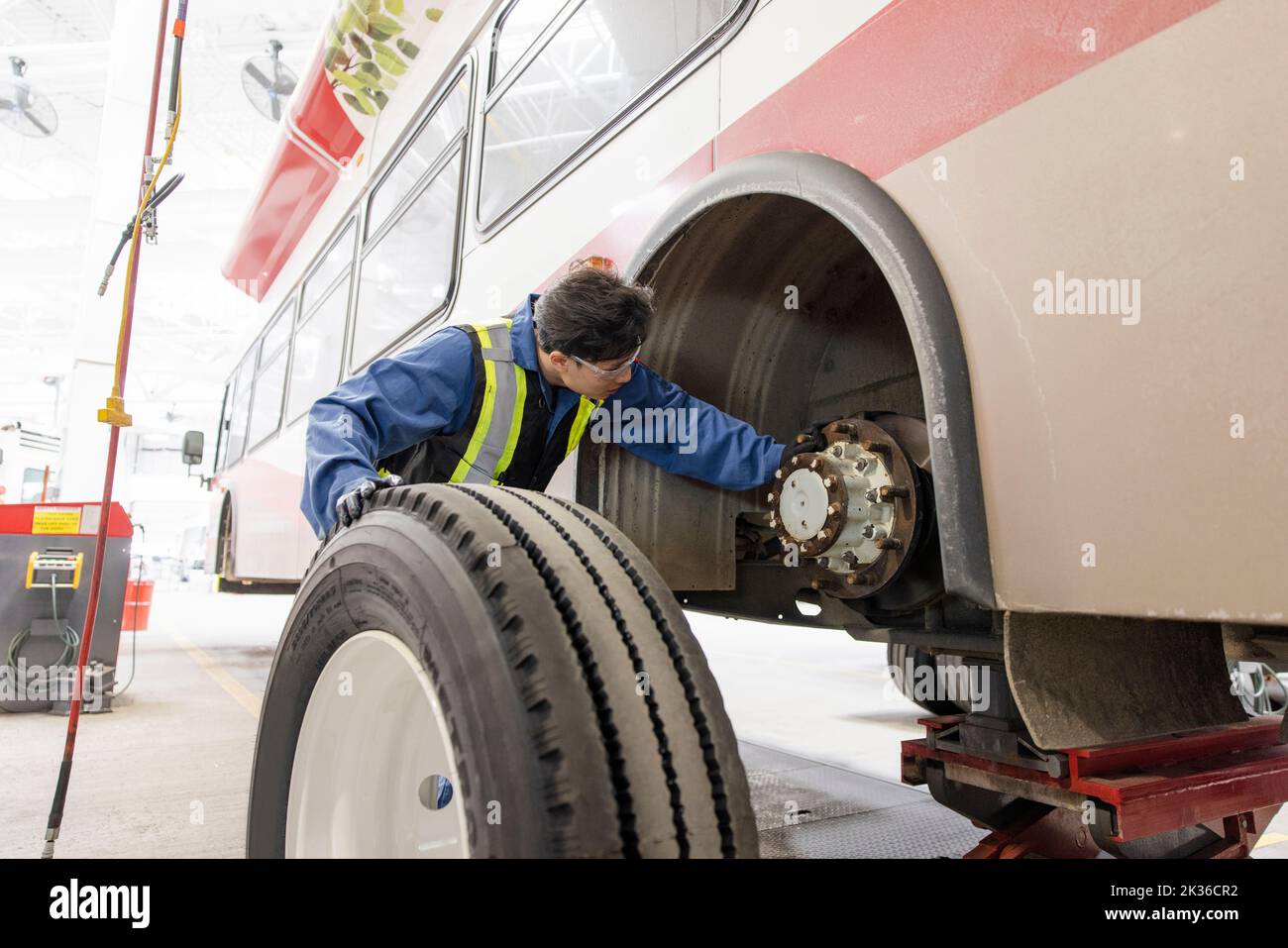 Male maintenance facility engineer replacing tire on bus Stock Photo