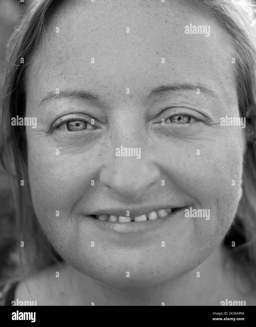 Close black and white portrait of a blond caucasian woman with bright eyes. She has a slight smile and a very positive aura Stock Photo