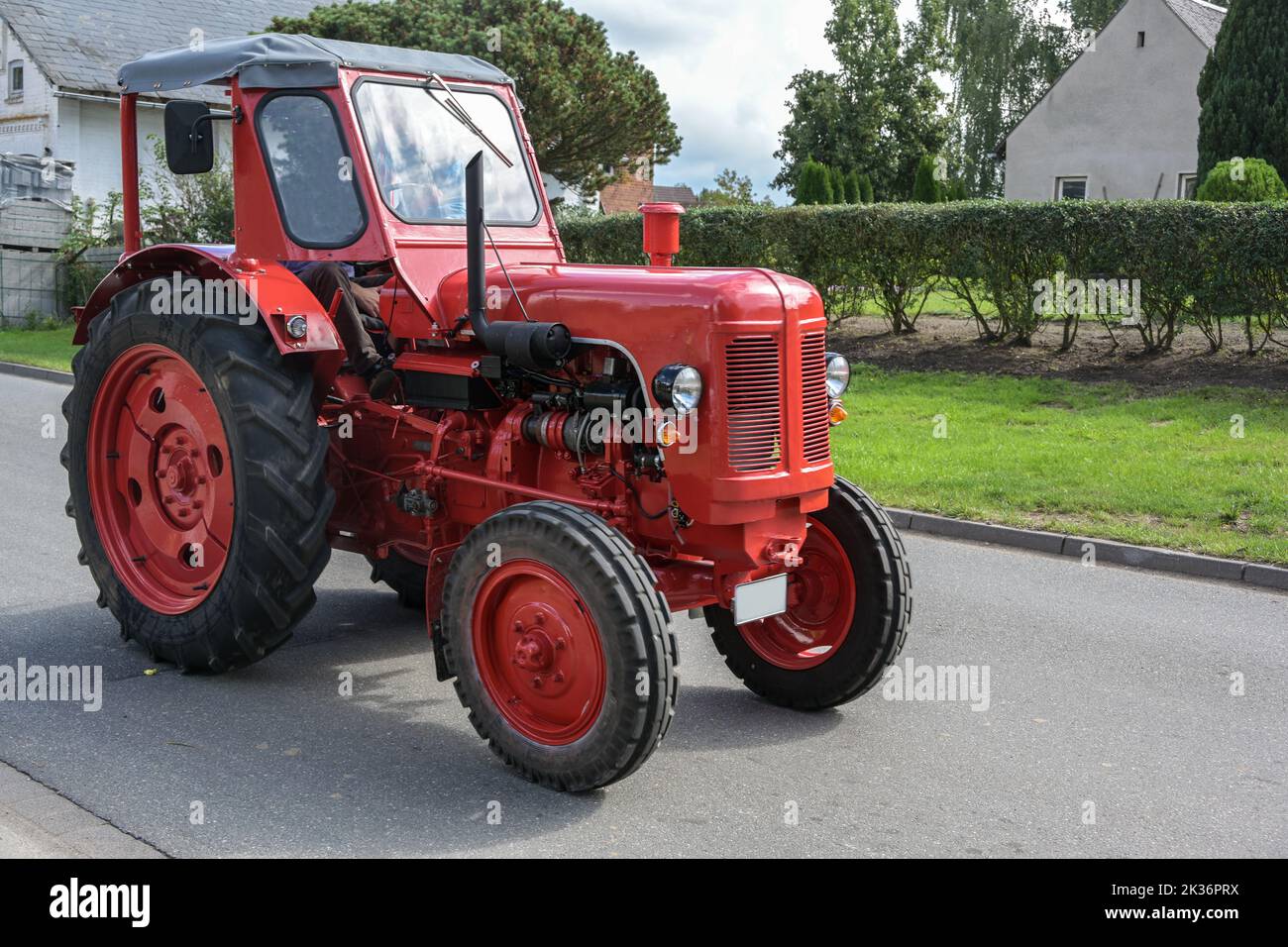 Red vintage tractor, carefully restored oldtimer, driving on the road through the village, motion bluer, selected focus Stock Photo
