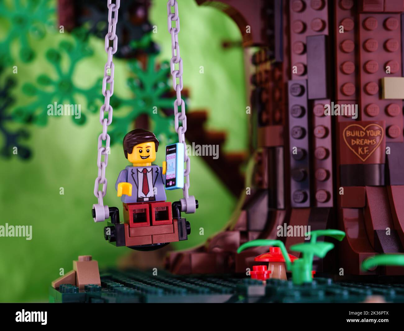 Tambov, Russian Federation - September 17, 2022 A Lego businessman minifigure sitting on a swing and holding his phone. Stock Photo