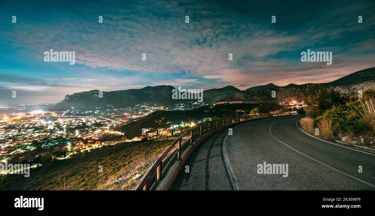 Terracina, Italy. Top View Skyline Cityscape City In Evening Night Illuminations. Night Open Road And Beautiful Cityscape. Panorama, Panoramic View Stock Photo