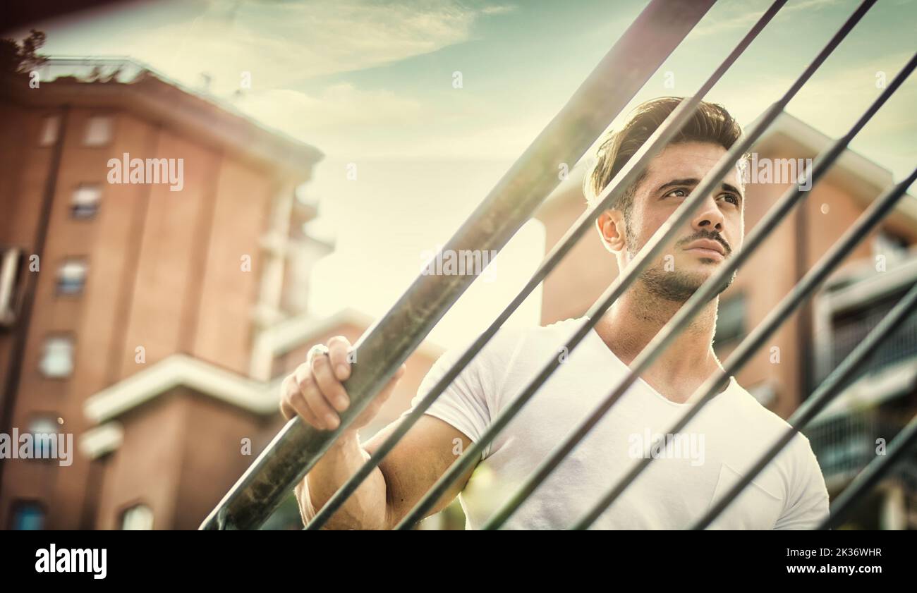 Handsome fit man in white t-shirt outdoor in city setting, climbing metal stairs, looking away Stock Photo