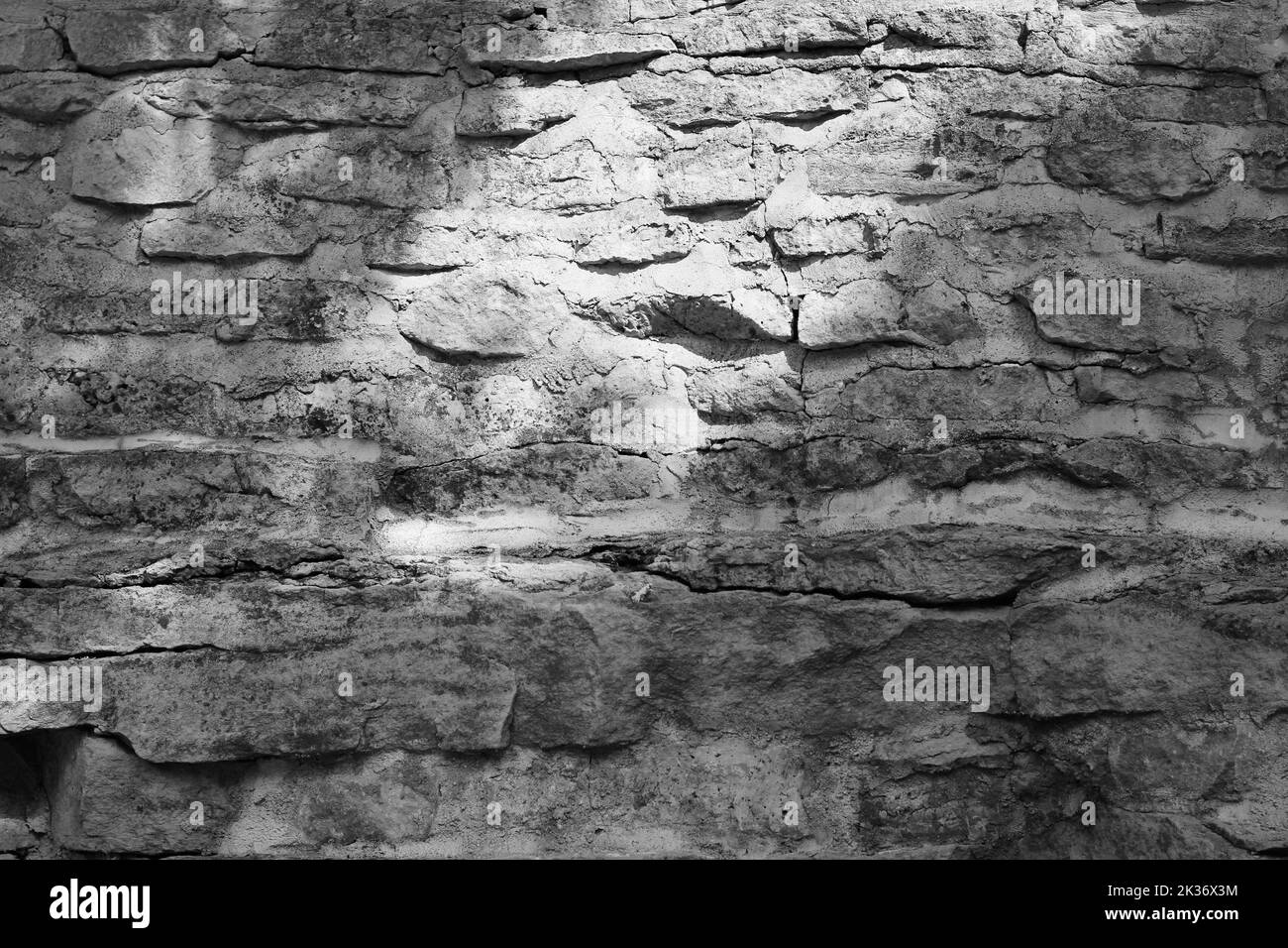 An old limestone stone wall with layers and cracks in a black and white