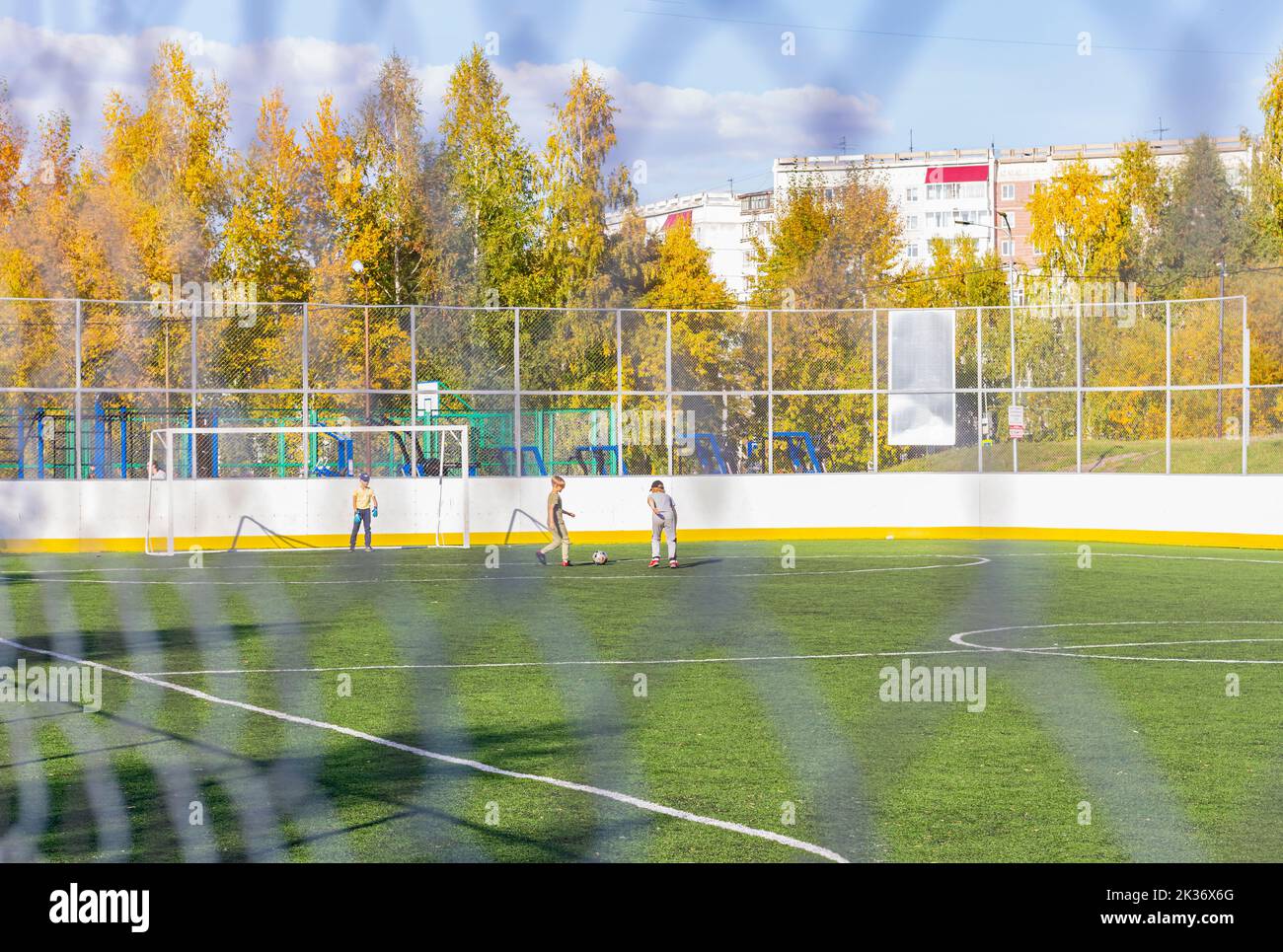 Young boys playing soccer game in golden autumn weather. Bright sun illuminates guys Tomsk Russia September 10, 2022.Blurred gray mesh with blurry boy Stock Photo