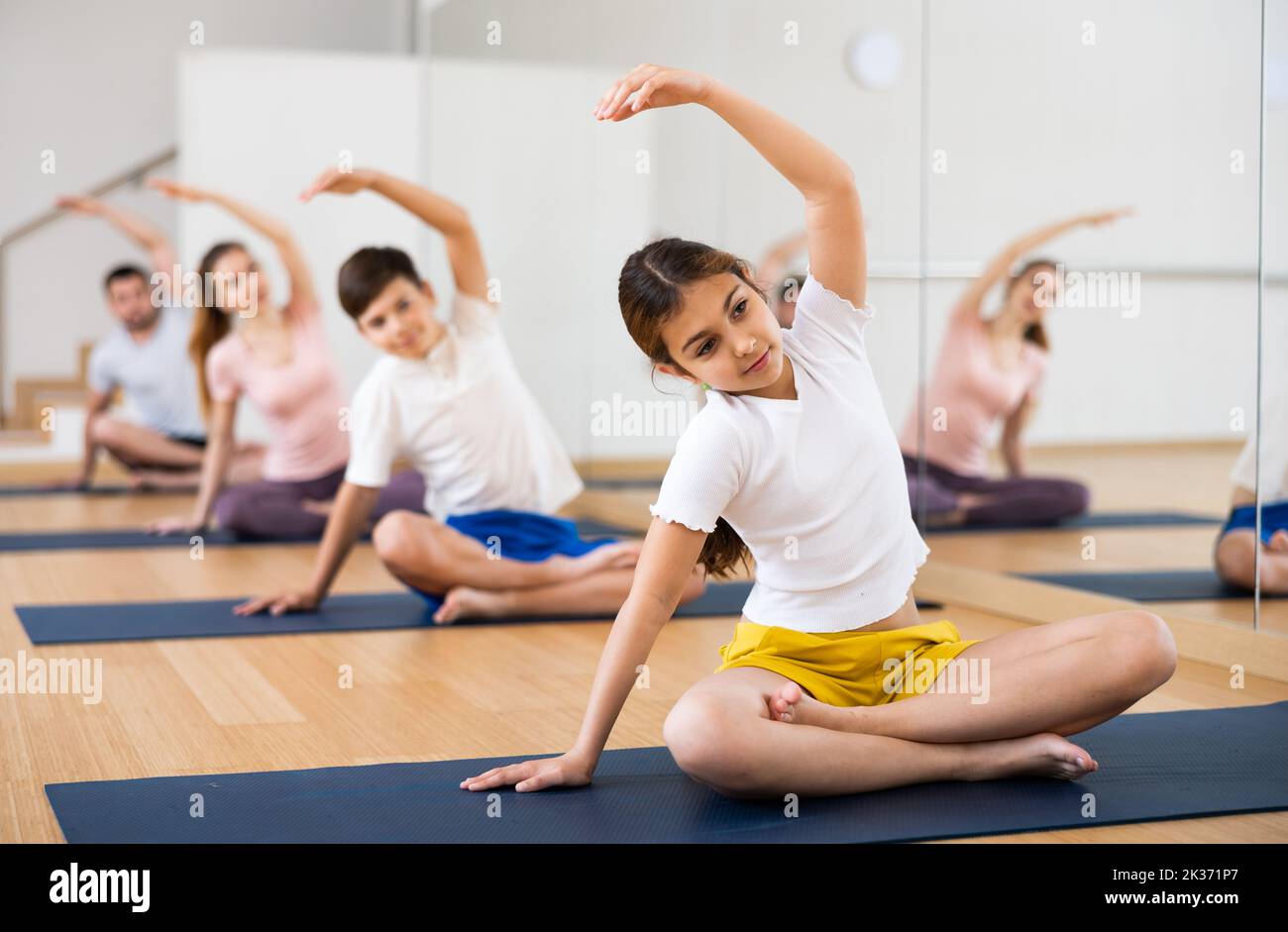 Girl sitting in lotus pose and stretching during training with family ...