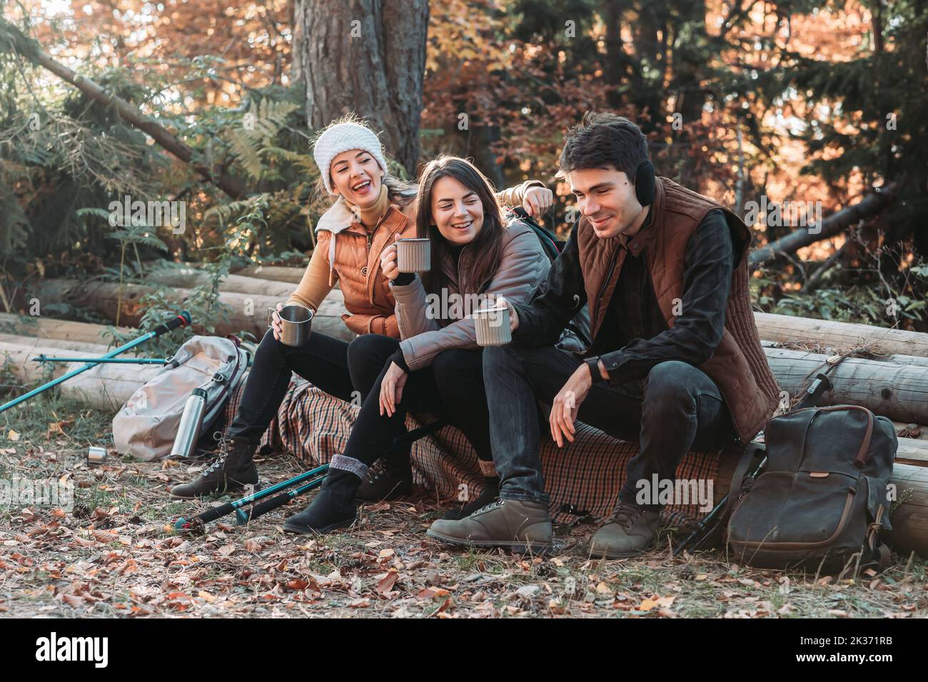 Three friends drinking tea outdoors in the nature, sitting on the trunk Stock Photo