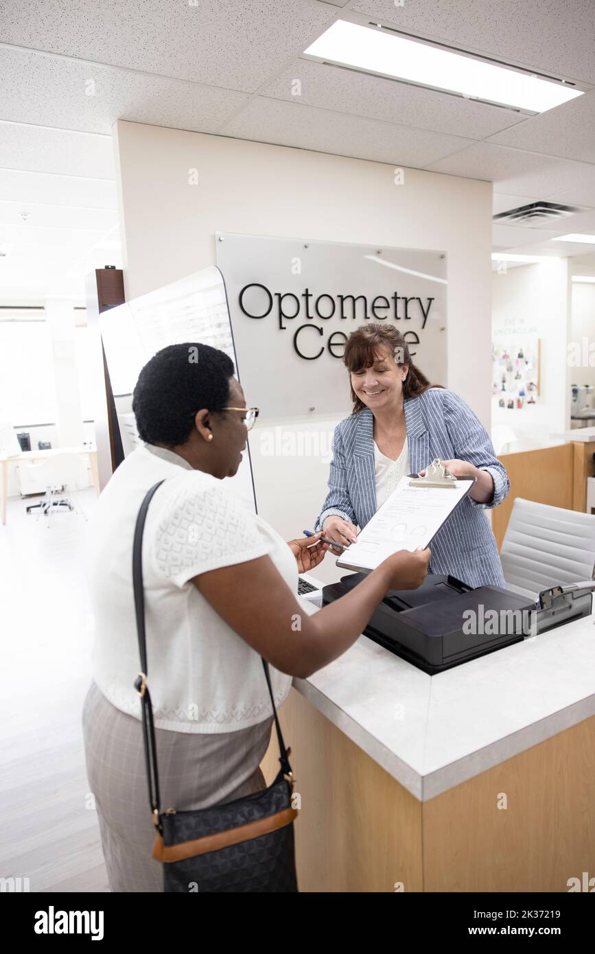 Female receptionist helping patient with paperwork in optometry center Stock Photo Alamy