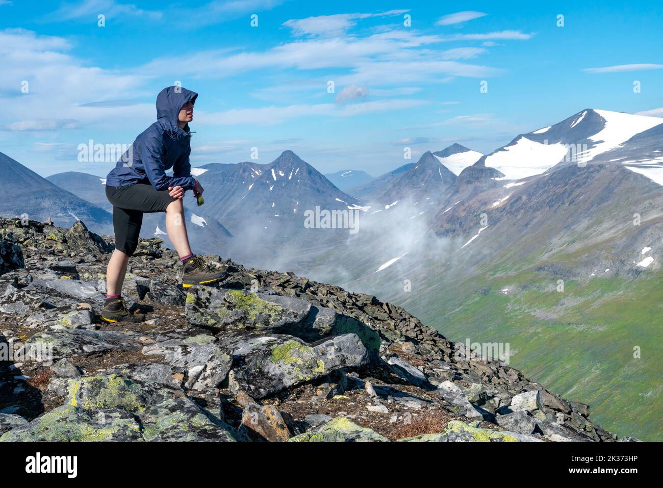 Female hiker in blue jacket overlooking vast arctic mountain landscape