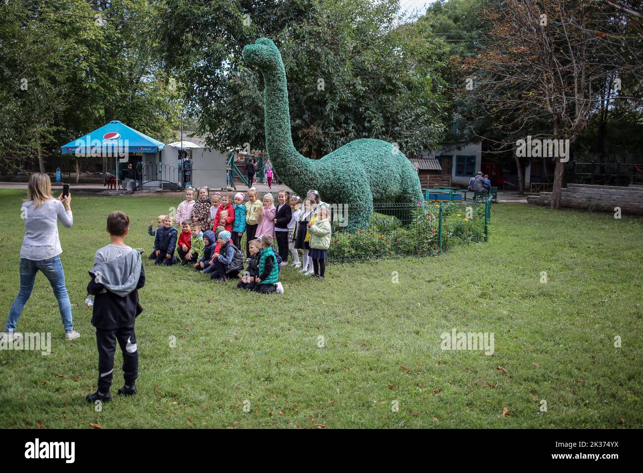 Children are seen taking pictures near the dinosaur figure. One of the oldest in Ukraine, the Odessa Zoo was established in September 1922 In honor of the centenary of the zoo, solemn events were held:1.? memorial plaque was opened to its first director Heinrich Beizert. 2.Ukrposhta issued a special envelope and a stamp. The circulation is limited, only 200 pieces. Stamp cancellation was carried out right at the zoo. 3.Together with the Odessa mayor Gennady Trukhanov, the director of the zoo, Igor Belyakov, opened a new lion cub.In April, a pair of white lions from the Feldman Ecopark in Khark Stock Photo