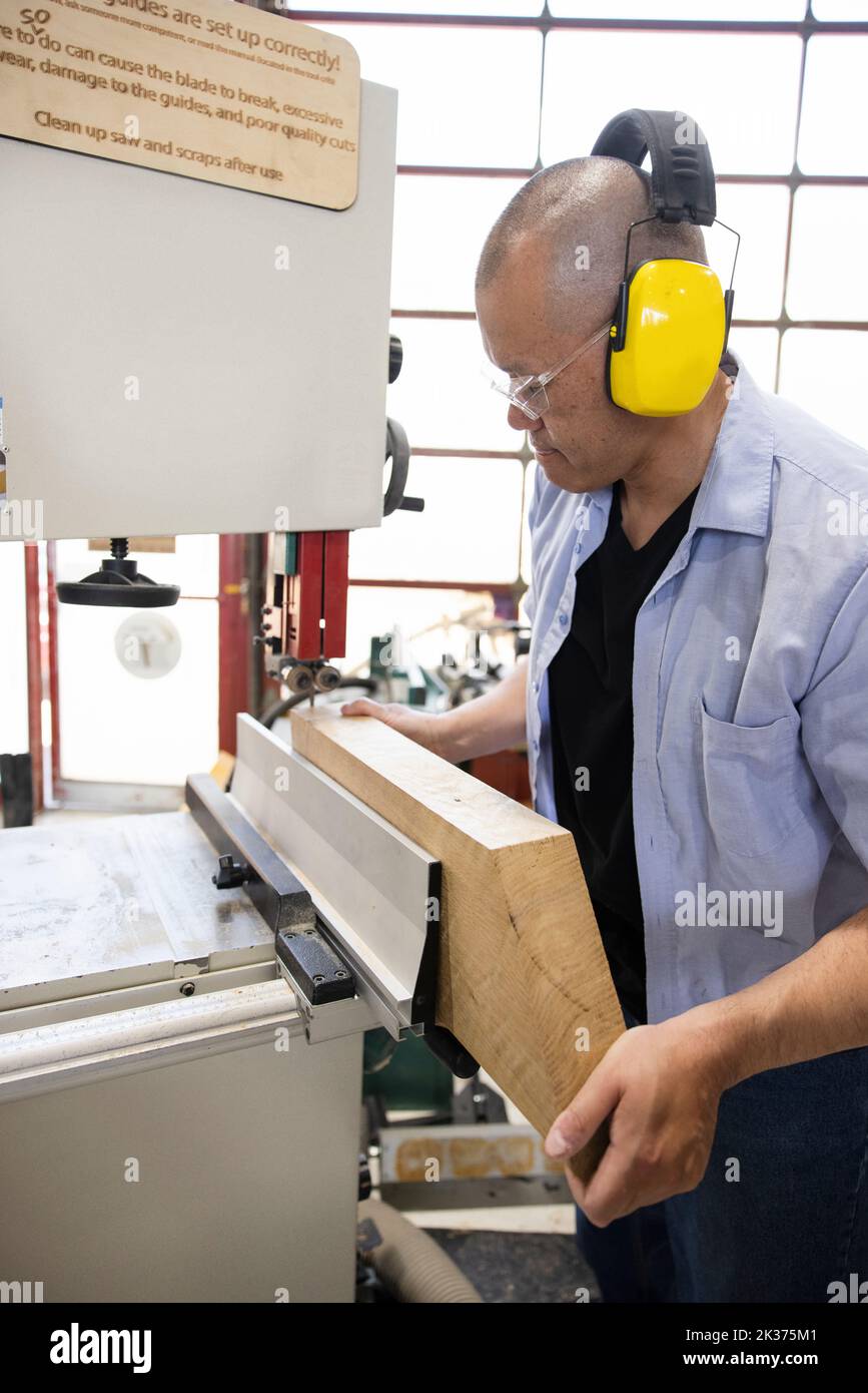 Woodworker with ear protectors using bandsaw in wood shop Stock Photo