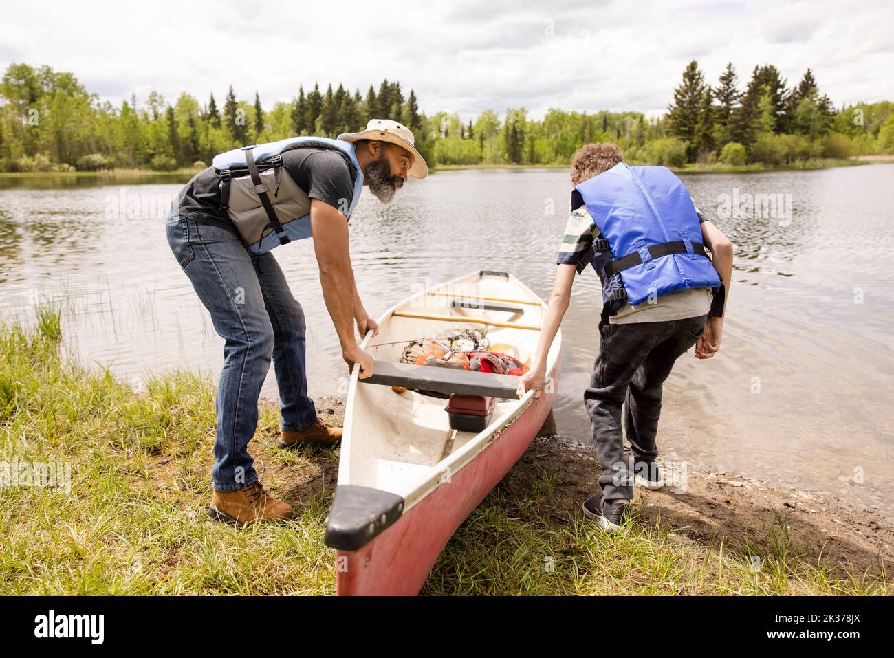 Father and son getting into canoe next to lake Stock Photo Alamy