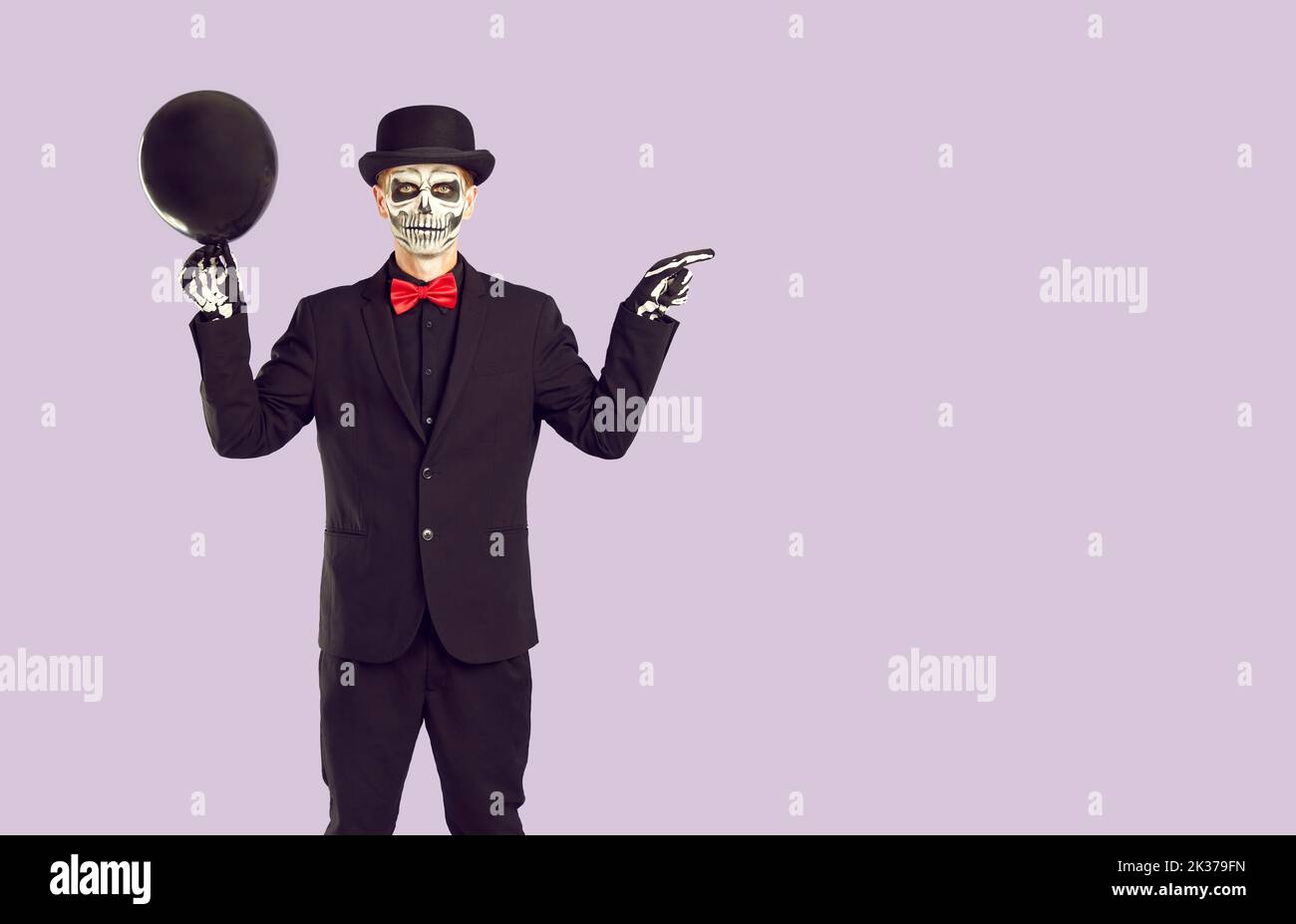 Man in skeleton Halloween costume shows something on light purple copy space background Stock Photo