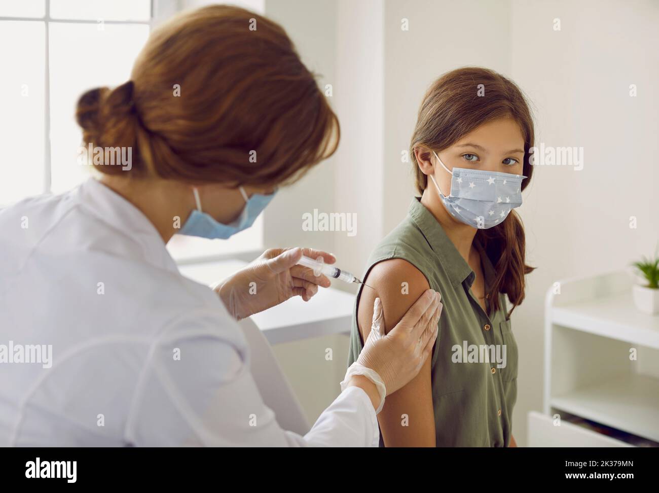 Nurse giving flu, covid or monkeypox vaccine injection to child patient in face mask Stock Photo