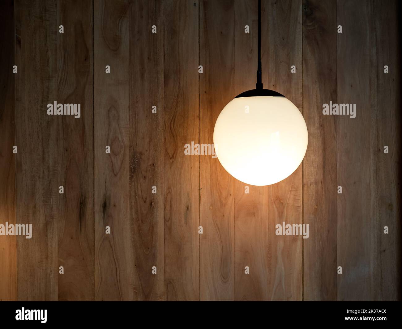 Round hanging lamp, full moon shape with the light bulb inside shining in the wood wall background in the dark room with copy space. Stock Photo
