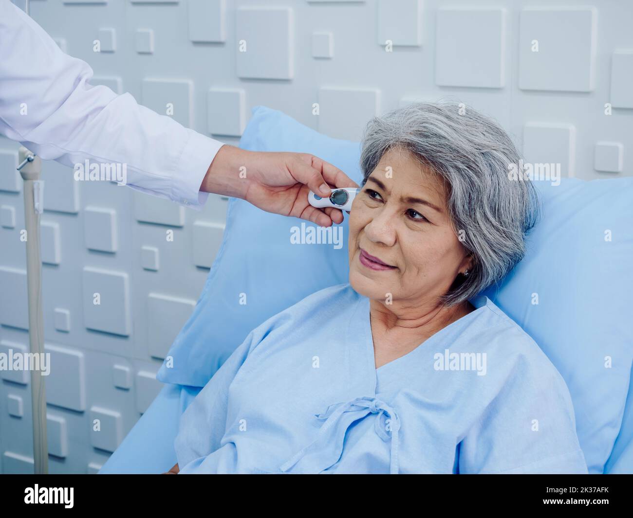 Portrait of Asian elderly woman patient on bed is being measured checked by temperature in the ear with tympanic thermometer by doctor in hospital or Stock Photo