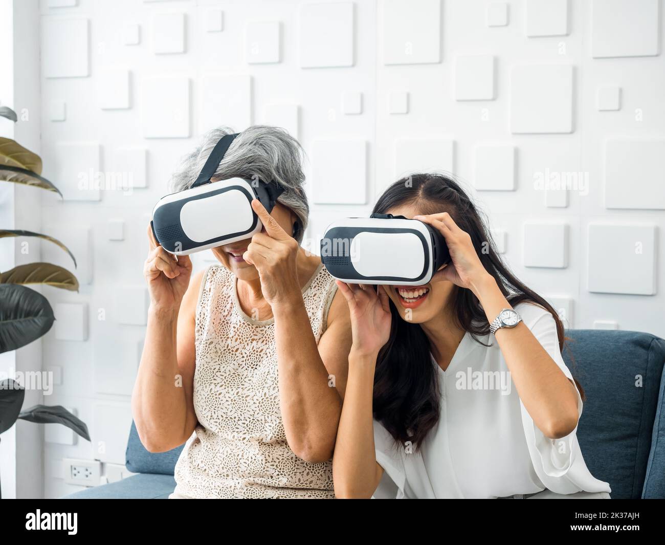 Asian young woman, happy daughter and her mother, old senior female wearing VR glasses, enjoy 3d game online together in white room. Mom and daughter Stock Photo