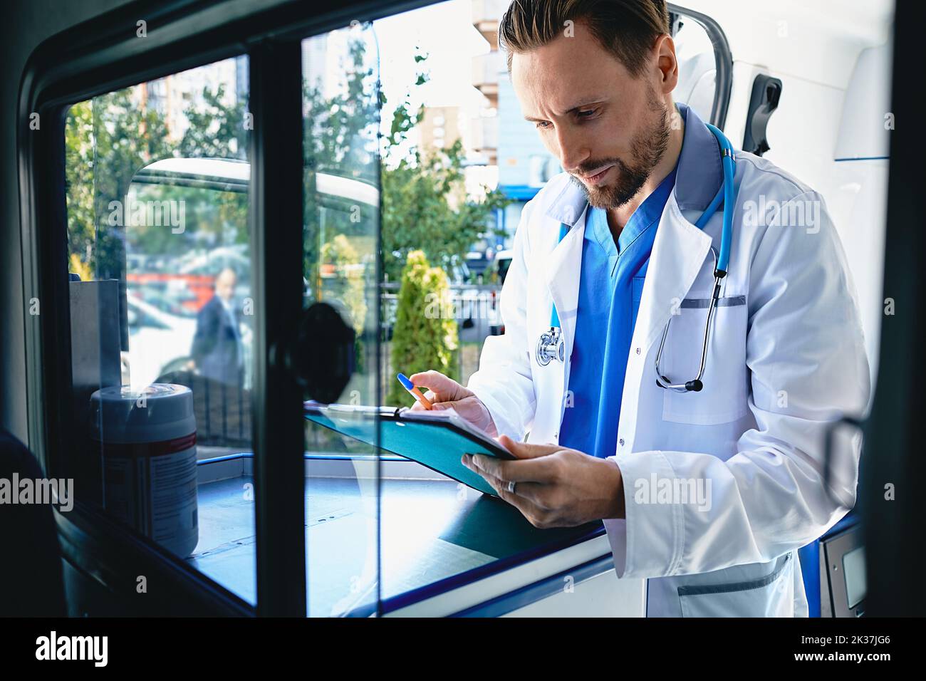doctor is filling out rescue questionnaire sitting in ambulance near patient and analyzing health indicators. Emergency medical services Stock Photo