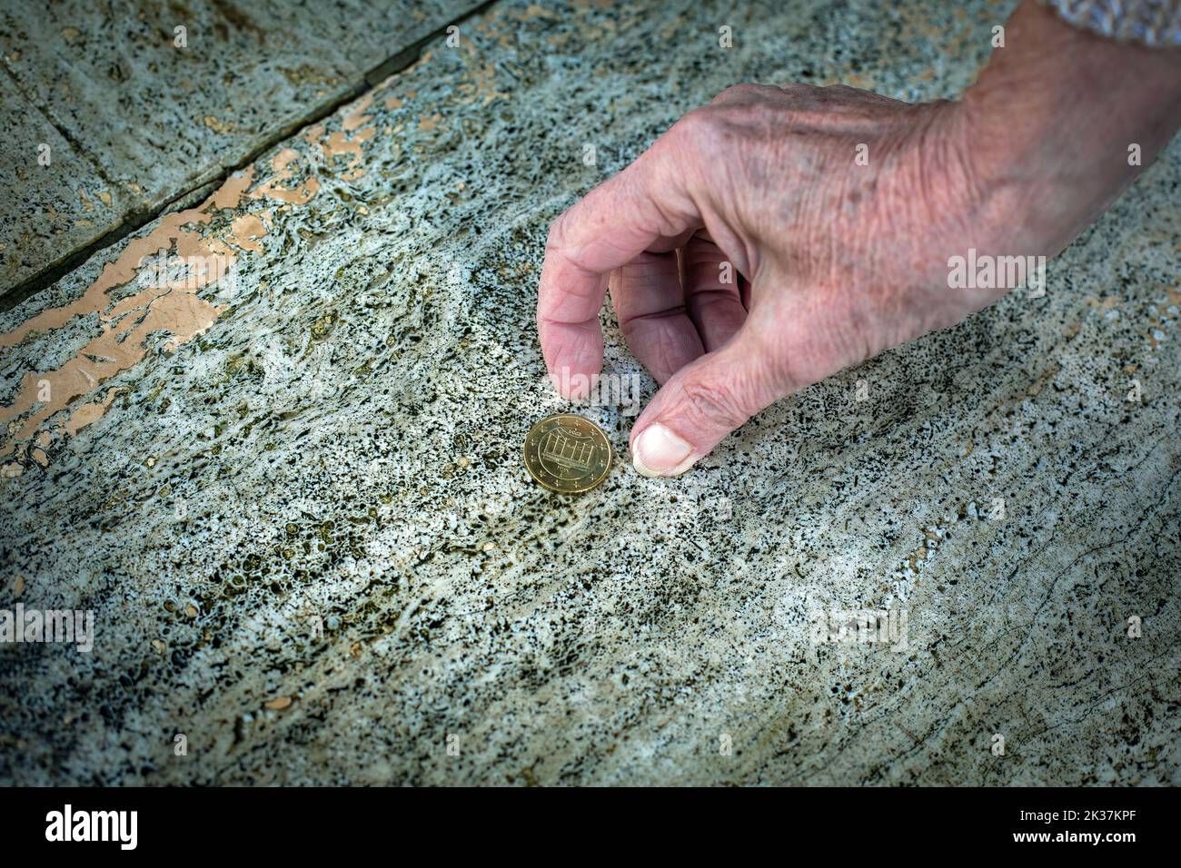 close-up of old womans hand picking up a coin from the floor Stock Photo