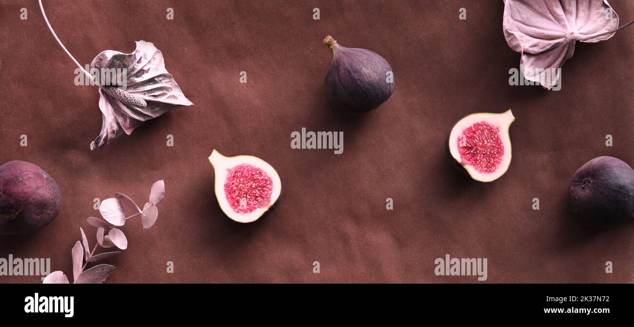 Fresh halved fig fruits and dry euvalyptus and cala lily flowers painted metallic pink on bstract textured background. Stock Photo