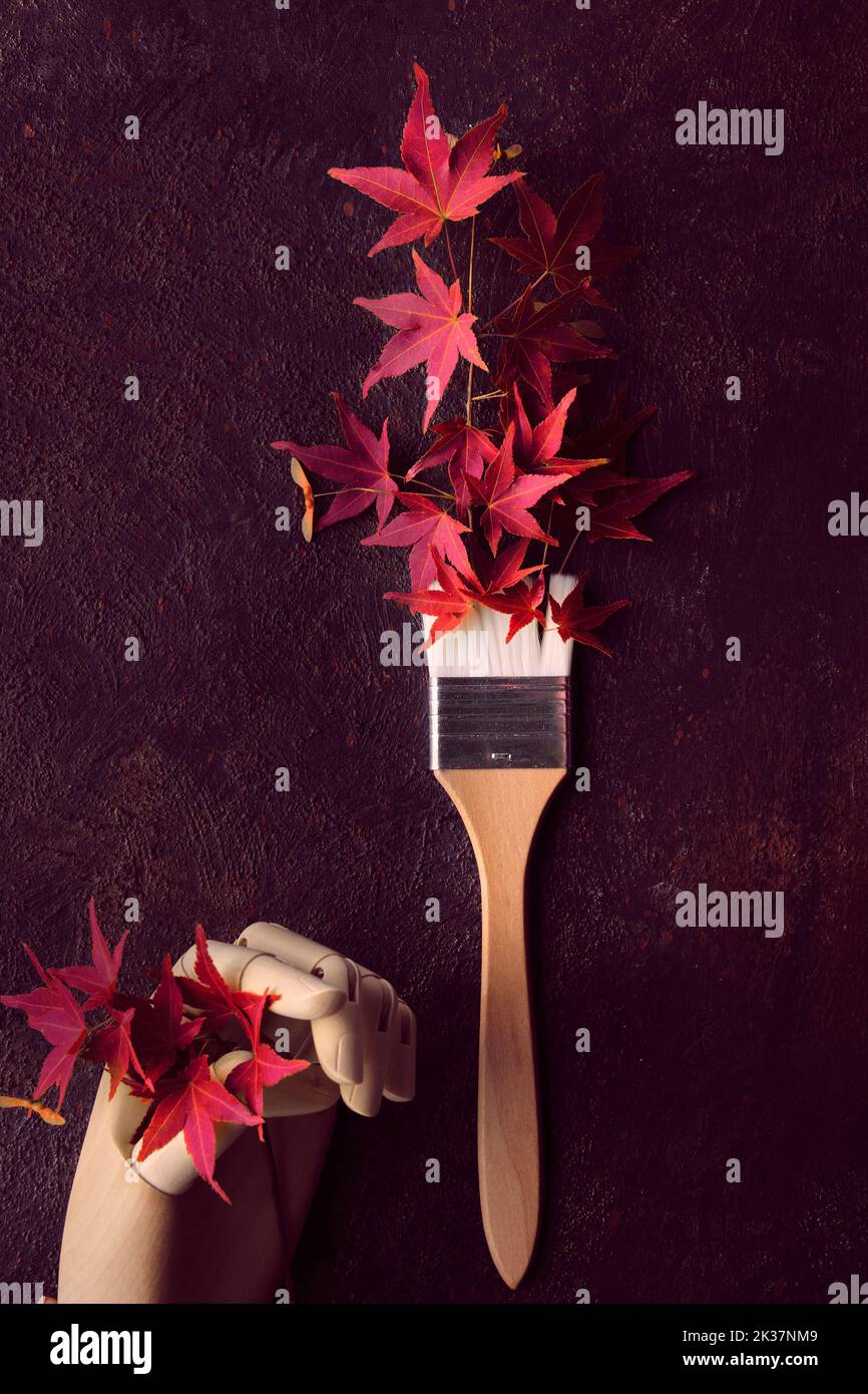 Paint brush, paintbrush with red oak leaves as paint. Red maple leaves in artistic model wooden hand. Autumntime colors, creative flat lay, top view. Stock Photo