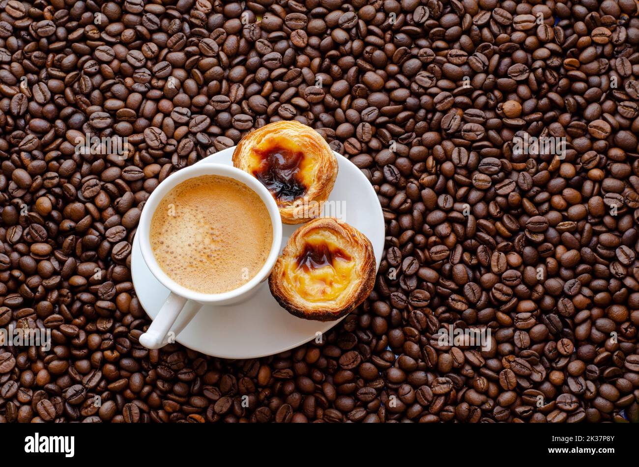 Coffee beans and a cup of hot espresso with foam, and two cakes. Stock Photo