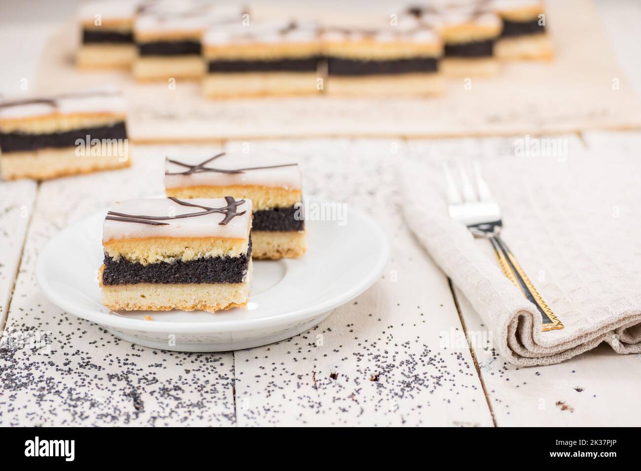 Poppy cake slices topped with sugar icing, decorated with melted chocolate. Pie name Berlin cake. Served on the white wooden table. Sweet dessert. Stock Photo