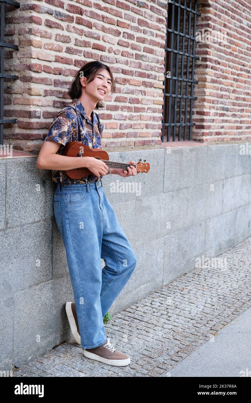 Asian guy smiling and playing acoustic Ukulele guitar. Stock Photo