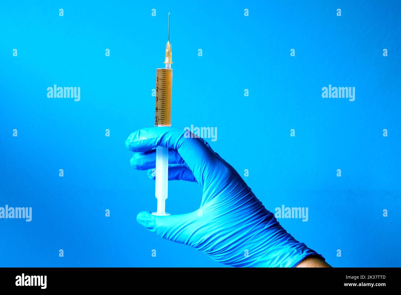 nurse hand in latex glove holding syringe wth orange liquid medicine