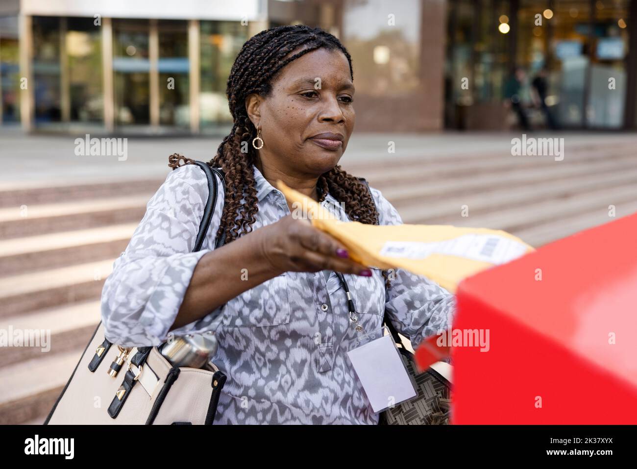 Woman with cornrow hair placing package into mailbox Stock Photo