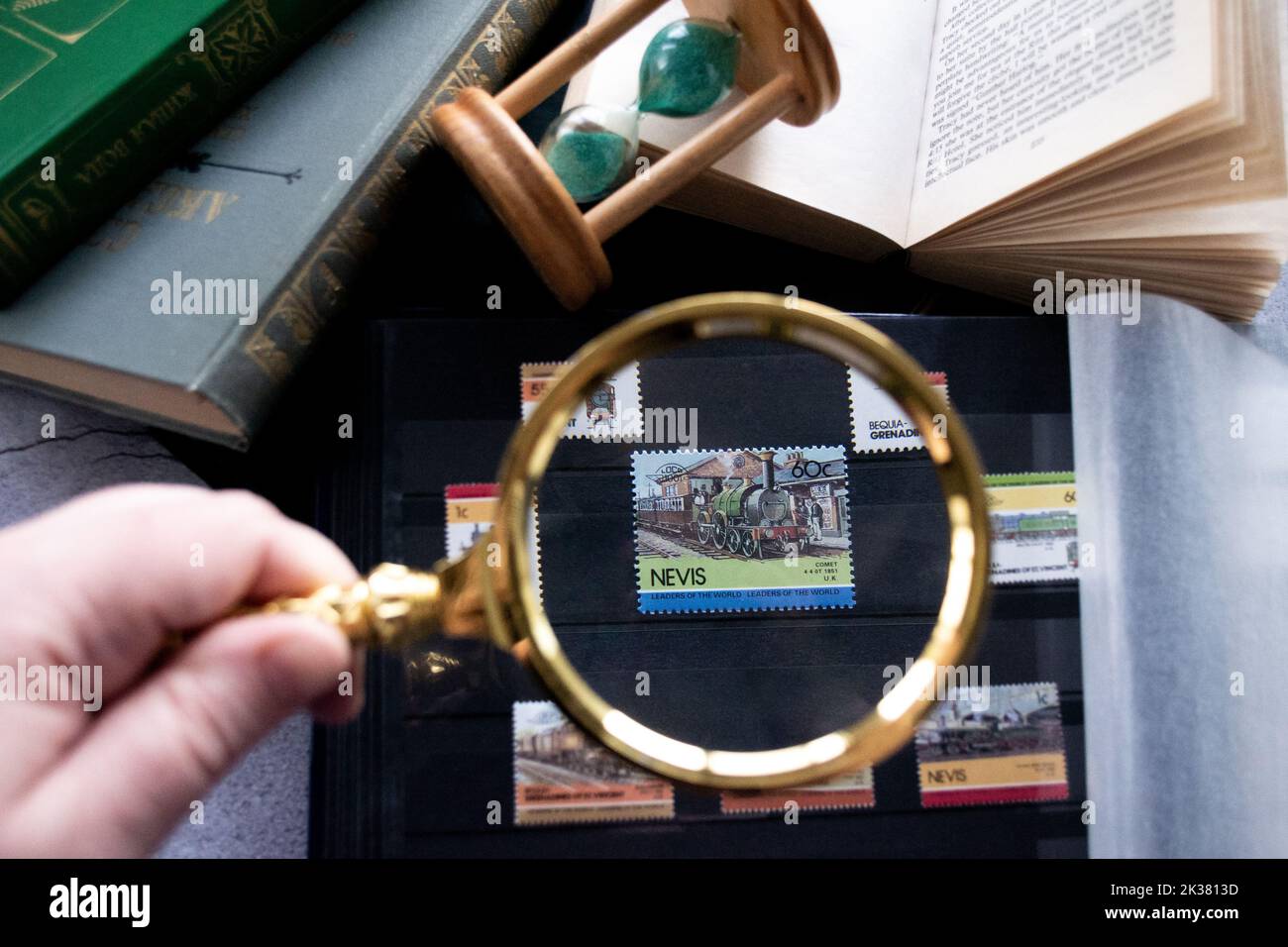 Moscow, Russia, March 2022: Hobby - stamp collecting. Looking at an 60 cent stamp of Nevis with locomotiv through a golden magnifying glass. Old books Stock Photo