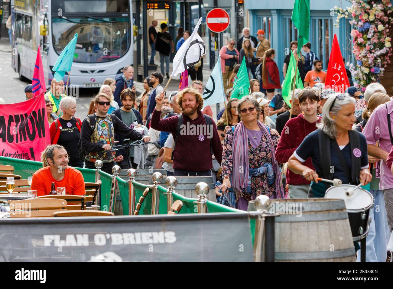 Bath, UK. 25th Sep, 2022. With PM Liz Truss signalling an acceleration of oil and gas extraction in the UK shoppers enjoying a drink look on as climate change protesters take part in a protest march through the centre of Bath. The protest organised by Extinction Rebellion was held in order to highlight how the cost of living crisis and the climate crisis are interlinked. Credit: Lynchpics/Alamy Live News Stock Photo
