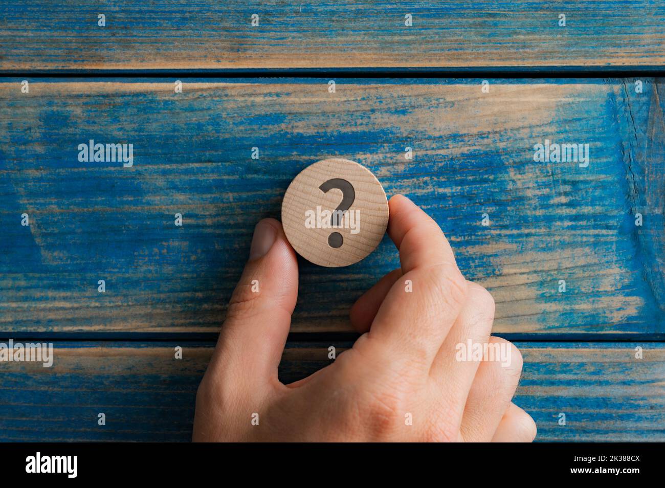 Male hand placing a wooden cut circle with a question mark on it over an aged blue background. Stock Photo