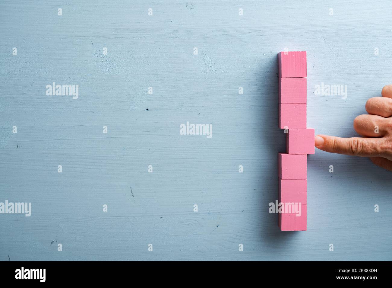 Male finger pushing a pink wooden block into a stack of them. Over blue background with plenty of copy space. Stock Photo