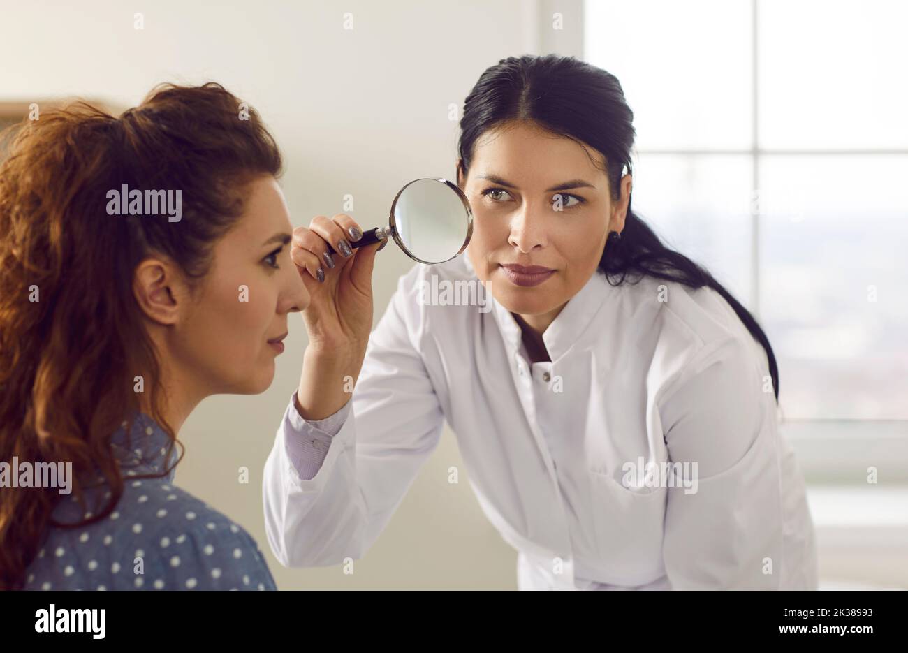 Dermatologist examines woman's face with magnifying glass and determines condition of her skin. Stock Photo