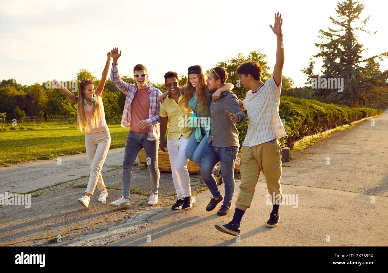 Cheerful and noisy company of young friends have fun walking along path walking in summer in park. Stock Photo