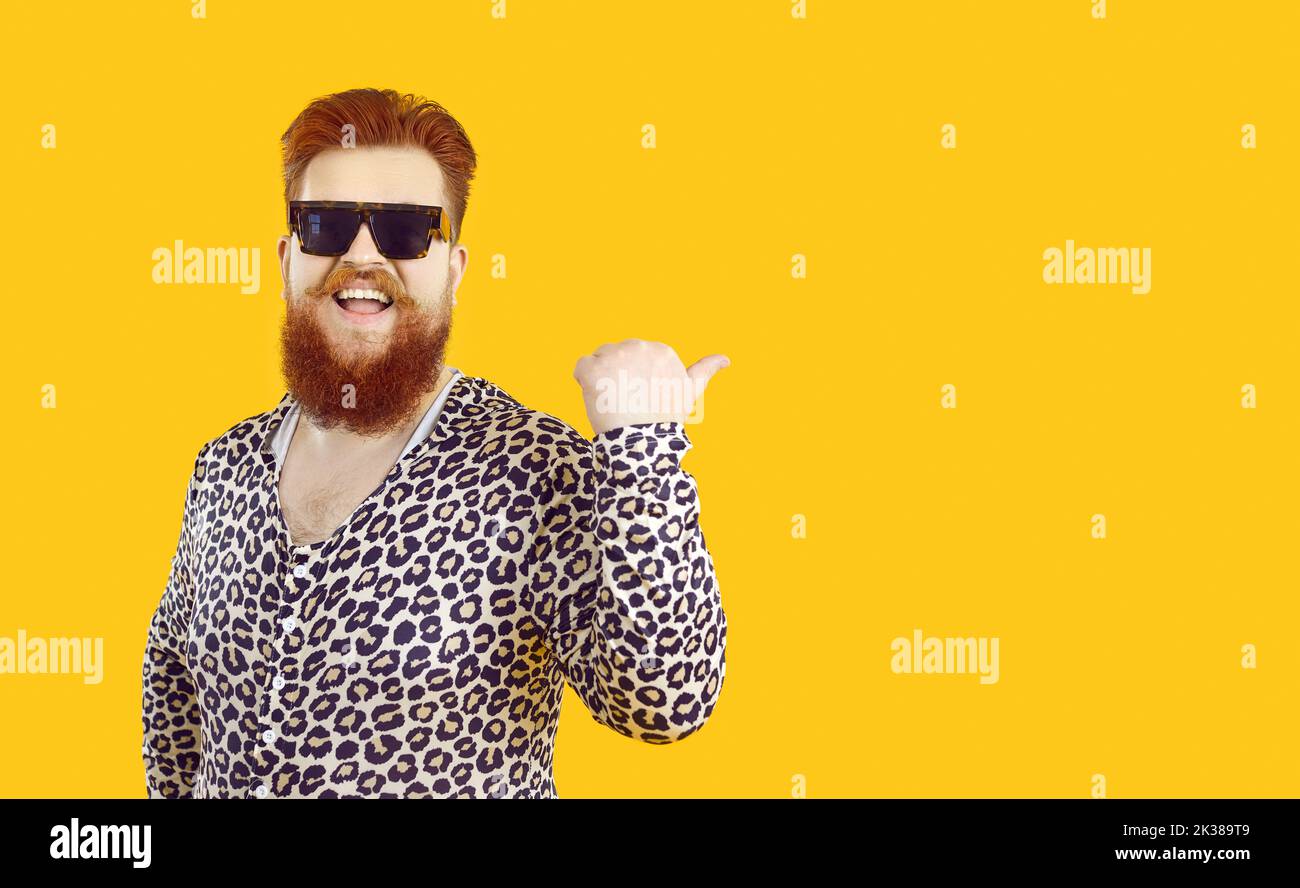Cheerful funny fat man points his thumb at copy space behind him on orange background. Stock Photo